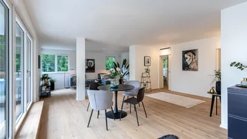 Helles, offenes Wohn-Esszimmer mit Holzboden, großen Fenstern und Zugang zum Außenbereich.