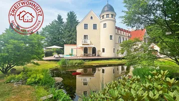 Elegantes Anwesen mit Turm, Teich und weitläufiger Terrasse, umgeben von üppigem Grün.