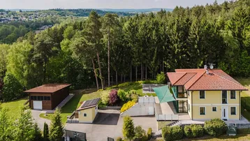 Luftaufnahme eines Hauses mit rotem Ziegeldach, umgeben von Wald und grüner Landschaft.