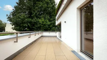 Geräumiger Balkon mit Fliesenboden, modernem Geländer und Blick ins Grüne.