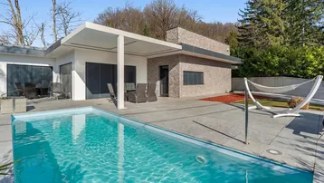 Moderne Villa mit Swimmingpool, großer Terrasse und Gartenbereich unter blauem Himmel.