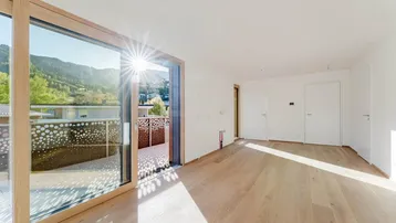 Helles Wohnzimmer mit Holzboden, großen Schiebetüren und Zugang zu einem sonnigen Balkon mit Bergblick.