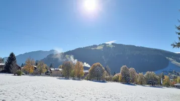Eine malerische Winterlandschaft mit schneebedeckten Feldern, Häusern und majestätischen Bergen unter strahlendem Sonnenschein.