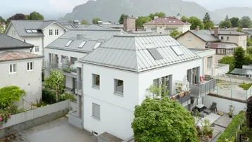 Modernes Mehrfamilienhaus mit Balkonen, Gartenbereich und beeindruckendem Bergblick im Hintergrund.