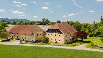 Großzügiger Gebäudekomplex mit gelben Fassaden und roten Ziegeldächern, eingebettet in grüne Landschaft.