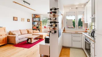 Helles, offenes Wohnzimmer mit Holzboden, gemütlichem Sofa und integrierter Küche mit Weinregal.