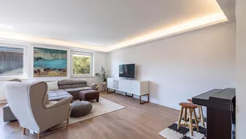 Helles Wohnzimmer mit modernem Sofa, Holzboden und indirekter Deckenbeleuchtung.