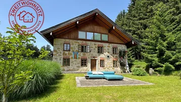 Traditionelles Steinhaus mit Holzelementen und großem Garten, umgeben von Wald und Natur.