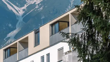 Moderne Wohngebäude mit Balkonen und beeindruckendem Bergblick, umgeben von grünen Bäumen.