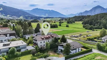 Luftaufnahme eines Gebäudes mit Bergblick, umgeben von grünen Feldern und Natur.