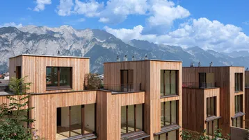 Moderne Reihenhäuser mit Holzfassaden und großen Fenstern vor einer beeindruckenden Bergkulisse.