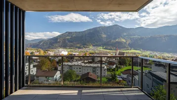 Geräumiger Balkon mit Glasbrüstung und weitem Blick auf die umliegende Berglandschaft und Stadt.