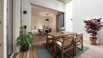 Helle Terrasse mit Holzboden und Sitzgelegenheiten, die zum Essbereich im Innenbereich führt.