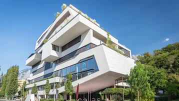 Modernes Gebäude mit markanter weißer Fassade, großen Fenstern und begrünten Terrassen in urbaner Umgebung.