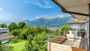Geräumiger Balkon mit Holzboden und Geländer, bietet einen weiten Blick auf die Berge und grüne Umgebung.