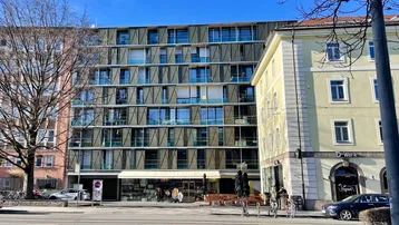 Modernes Gebäude mit vielen Fenstern und Balkonen an einer belebten Straße.