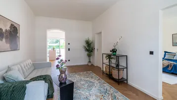 Helles Wohnzimmer mit modernem Sofa, Teppich und offenem Zugang zu einem weiteren Raum.