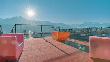 Sonnige Dachterrasse mit bunten Sitzgelegenheiten und einem atemberaubenden Bergblick.