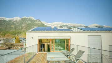Sonnige Dachterrasse mit Holzboden, Gartenmöbeln und beeindruckendem Bergblick.