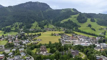 Panoramablick auf eine malerische Stadt im Tal, umgeben von grünen Bergen und Wäldern.