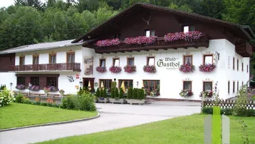 Traditionelles Gasthofgebäude mit blumengeschmückten Balkonen und gepflegter Außenanlage, umgeben von Wald.