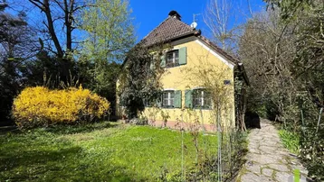 Gelbes Haus mit grünen Fensterläden und einem blühenden Garten unter blauem Himmel.