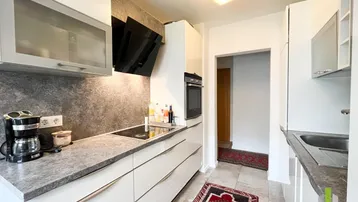 Moderne Einbauküche mit weißen Hochglanzfronten, grauer Arbeitsplatte und integrierten Geräten.