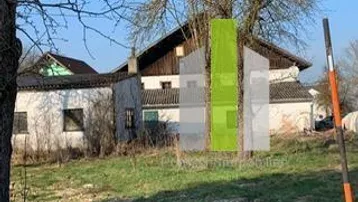 Altes Gebäude mit ländlichem Charme und großem Baum im Vordergrund, umgeben von Grasland.