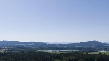 Weitläufige Landschaftsaufnahme mit sanften Hügeln, einem See und einem klaren blauen Himmel.