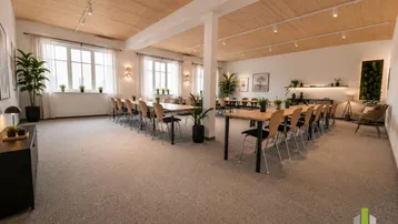 Großer Konferenzraum mit Holzbalkendecke, Teppichboden und viel Tageslicht durch hohe Fenster.