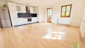 Helles, offenes Wohnzimmer mit integrierter Küche, Holzboden und Zugang zum Balkon.