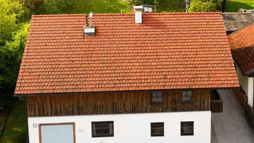 Luftaufnahme eines traditionellen Hauses mit rotem Ziegeldach und Holzfassade, umgeben von grünen Feldern.