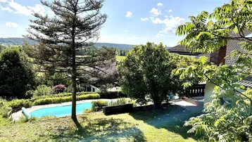 Großer Gartenbereich mit Pool, umgeben von üppigem Grün und weitem Blick in die Landschaft.
