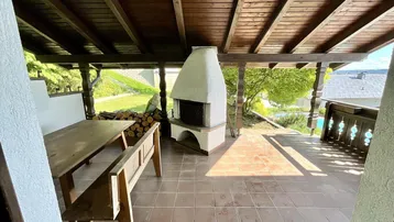 Überdachte Terrasse mit rustikalem Holztisch, Außenkamin und Blick ins Grüne.