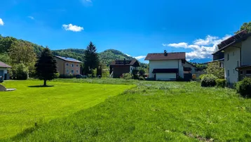 Weitläufige Grünfläche mit umliegenden Häusern und Bergblick unter blauem Himmel.