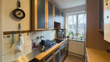 Funktionale Küche mit Holz- und blauen Schränken, Fliesen und einem Fenster mit Blick ins Grüne.