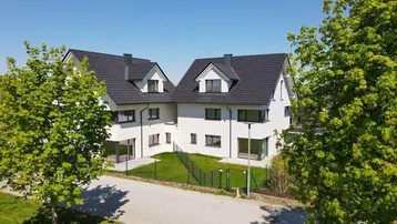 Zwei moderne Doppelhaushälften mit weißer Fassade und dunklem Satteldach in ländlicher Umgebung.