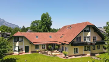 Großzügiges Haus mit gelber Fassade, rotem Satteldach und weitläufigem Garten mit Bergblick.