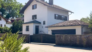 Weißes Einfamilienhaus mit Satteldach, integrierter Garage und Steinmauer im Vorgartenbereich.