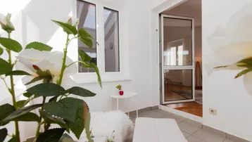 Heller Balkon mit Fliesenboden, weißer Sitzgelegenheit und Zugang zu einem Innenraum.