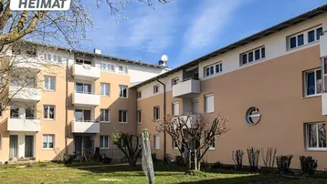 Mehrfamilienhaus mit moderner Architektur, Balkonen und einer gepflegten Grünfläche im Vordergrund.