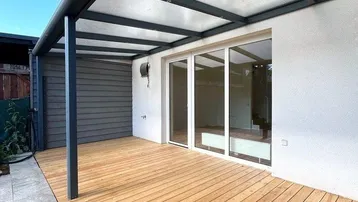Überdachte Holzterrasse mit direktem Zugang zum Innenbereich, ideal für entspannte Stunden im Freien.