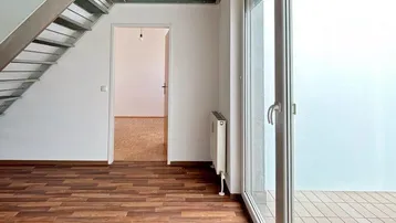 Heller Wohnbereich mit Holzoptikboden, offener Treppe und Zugang zur Loggia.