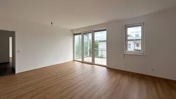Geräumiger, heller Wohnbereich mit Laminatboden und Zugang zu einem Außenbereich sowie einem weiteren Fenster.