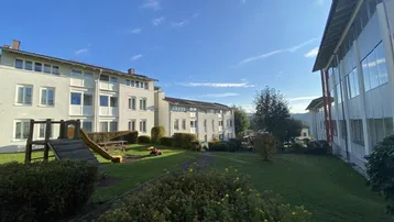 Mehrere Wohngebäude mit gepflegter Grünfläche und einem kleinen Spielplatz unter blauem Himmel.