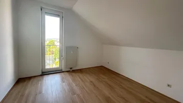 Helles Schlafzimmer mit Dachschräge, Laminatboden und Zugang zu einem französischen Balkon.