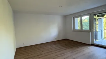 Helles Zimmer mit Laminatboden, weißen Wänden und Zugang zu einem Balkon.