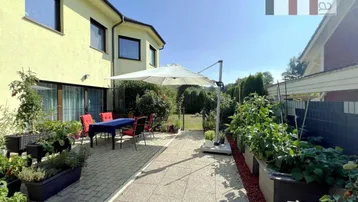 Sonniger Terrassenbereich mit Gartenmöbeln, Sonnenschirm und Hochbeeten für den Anbau von Gemüse.