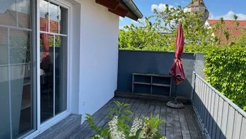 Holzdeck-Balkon mit Blick auf einen historischen Turm und viel Grün.