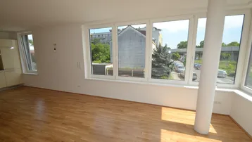 Helles Wohnzimmer mit Parkettboden und großen Fenstern, die viel Tageslicht hereinlassen.